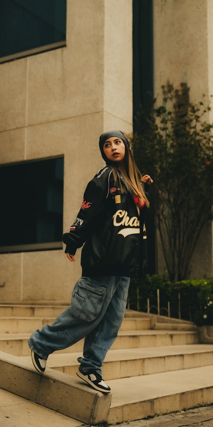 Stylish woman in streetwear poses confidently on urban steps, showcasing modern fashion.